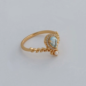 Detail of a pear-shaped blue topaz ring with gold leaf texture and a small white pearl