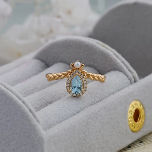Macro detail of gold pear-shaped blue topaz ring with pearl and wheat texture band