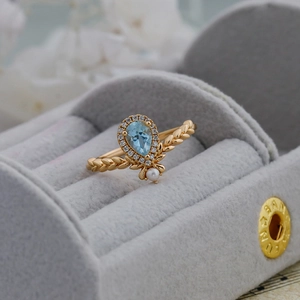 Detail of pear-cut sky blue topaz ring with diamond halo and pearl on leaf-textured band