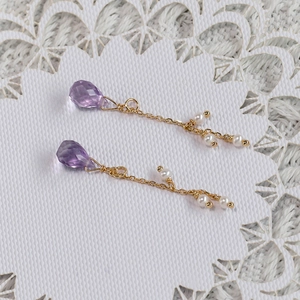 Dettaglio di orecchini di ametista con catene d'oro e piccole perle su pizzo
