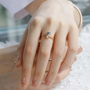 Detail view of vine leaf gold ring with blue topaz gemstone on white lace background