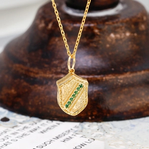 Macro-opname van een vintage gouden schildhanger met groene edelstenen en fijne gravures