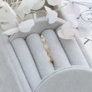 Macro detail of gold marquise ring with opal and stones on grey velvet background
