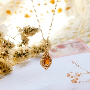 Close-up of S925 gilded petal pendant with orange garnet on a vintage floral background