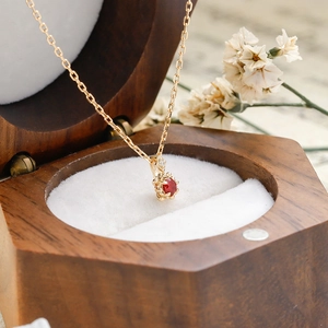 Gros plan d'un pendentif rubis rouge sur chaîne en or dans un coffret en bois
