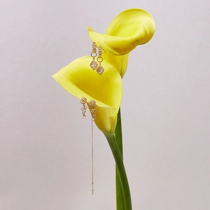 Détail de boucles d'oreilles dorées avec nœud et pompon sur une fleur de calla