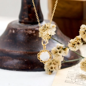 Gros plan d'un pendentif double face en nacre blanche avec détails floraux dorés fins