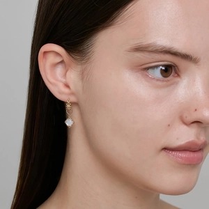 Détail de boucles d'oreilles pendantes dorées avec nacre naturelle sur un mannequin