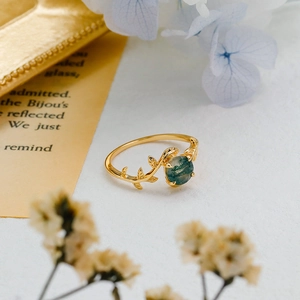 Detailed view of moss agate stone on a gold vine ring with leaves and floral backdrop