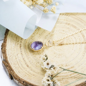 Dettaglio del ciondolo in ametista su catena in argento placcato oro 14K su base in legno