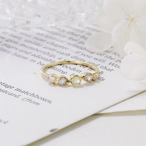 Detalle de anillo dorado con cinco piedras preciosas sobre fondo de tarjeta blanca