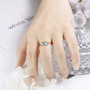Detail view of gold ring with three light blue gemstones and diamond accents on finger