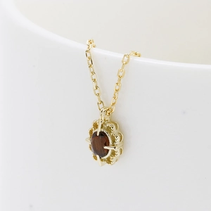 Detail of s925 gold necklace featuring a flower pendant with dark oval gemstone