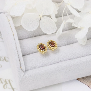 Macro detail of garnet stud earrings with golden lace bezel on grey velvet box