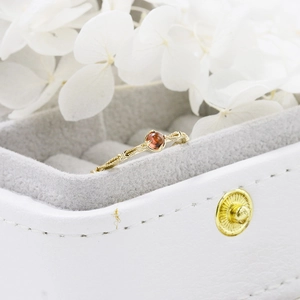 Macro detail of garnet ring with twisted gold band set in a white leather jewelry box