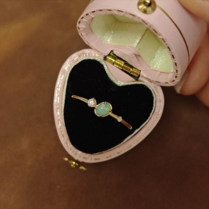 Anillo de oro con ópalo y piedras laterales en un joyero rosa de corazón