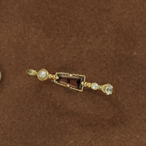 Makroaufnahme eines goldenen Vintage-Rings mit rotem Edelstein, Perle und Zirkonia