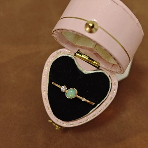 Macro detallada de un anillo de opalo ovalado dorado en un joyero rosa de corazón