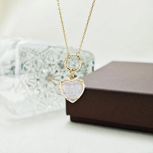 Detalle de un colgante de corazón dorado con calavera y anillo de diamantes en cadena fina