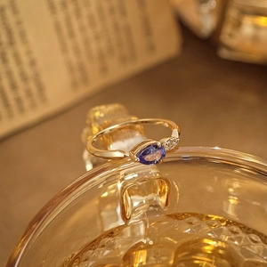 Vue macro d'une bague dorée avec tanzanite en forme de poire sur un bord de verre