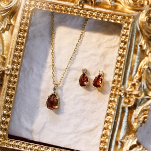Elegant gold necklace and teardrop garnet earrings set in a vintage ornate frame