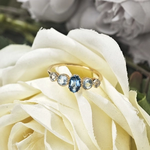 Close-up of gold ring with five blue topaz stones nestled in a white rose flower