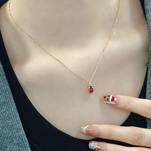 Close-up of a pear-shaped red garnet necklace pendant on a minimalist gold chain
