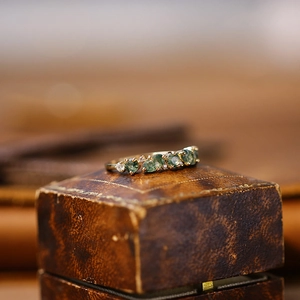 Macro shot of gold moss ring featuring five green gemstones and tiny white diamonds