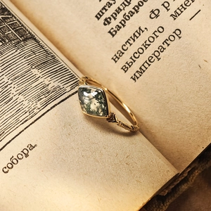 Detailed view of a vintage rhombus moss agate ring on a gold band set against a book