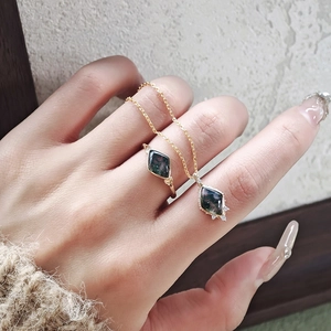Close-up of moss agate jewelry set in gold including rhombus ring and pendant necklace