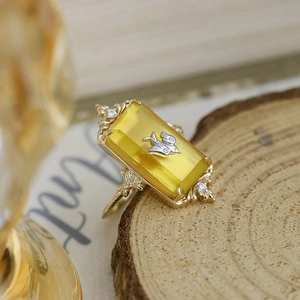 Vintage gold ring with rectangular yellow gemstone and silver bird detail on wood