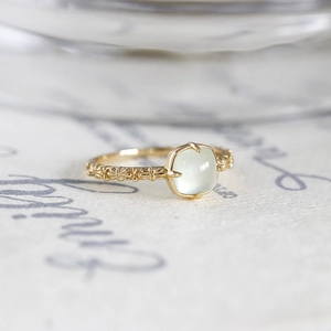 Macro detail of gold vintage ring with light green square stone and carved band