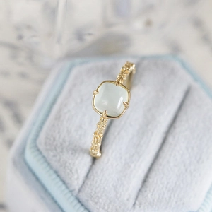Macro shot of square pale green gemstone set in gold-plated ring on velvet box