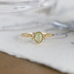 Detail of pear-cut peridot ring featuring golden leaf carvings and vintage claw setting
