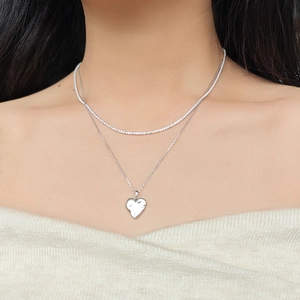 Close-up of a layered silver heart pendant necklace worn by a model on a white knit sweater