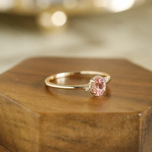 Close-up of an oval pink gemstone ring on a walnut wood stand with elegant lighting