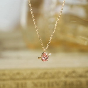 Macro view of gold necklace with oval pink gemstone and diamond-studded arrow pendant