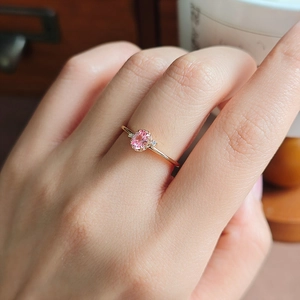 Close-up of pink oval gemstone ring with side diamonds on a rose gold band