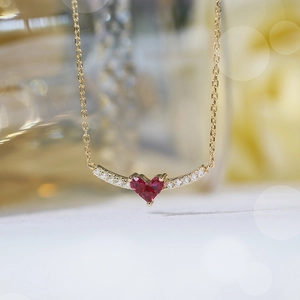 Macro shot of V-shaped gold necklace featuring ruby heart pendant and diamond accents