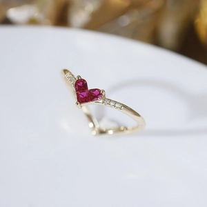 Macro detail of V-shaped gold ring with heart-shaped red rubies and side diamonds