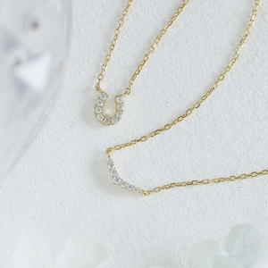 Macro view of gold U-shaped horseshoe pendant and curved diamond necklace set