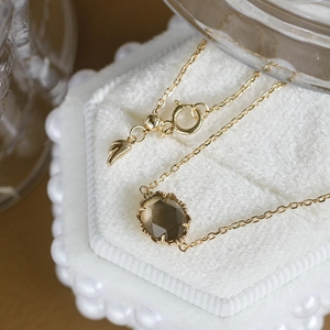 Lujoso collar dorado con cuarzo ahumado y colgante de ala sobre un joyero muy elegante