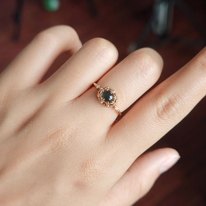 Close-up of gold-plated ring featuring an oval green stone and vintage hollow frame detail