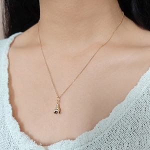 Gouden ketting met Eiffeltoren-hanger gedragen door een model op een beige achtergrond