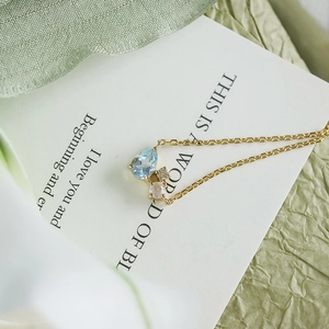 Close-up of gold necklace featuring sky blue teardrop and pink round gemstone pendants