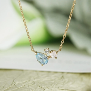 Macro view of gold-plated necklace with pear-shaped blue topaz and pink gemstone detail