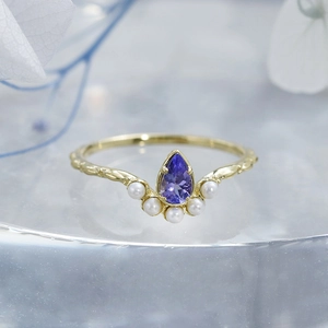 Détail macro d'une bague couronne en or avec tanzanite violette et cinq perles blanches