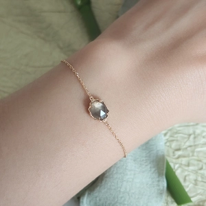 Detalle de una pulsera de oro minimalista con un dije de cuarzo ahumado facetado