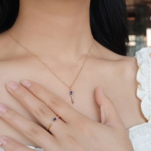 Detail van vergulde S925 zilveren sleutelketting en blauwe saffierring gedragen op model