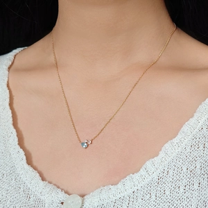 Close-up of a gold necklace with blue topaz and diamond pendant on a female model